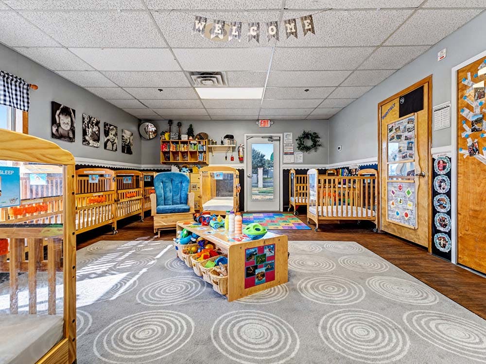A classroom with cribs, play area, and decor on the walls