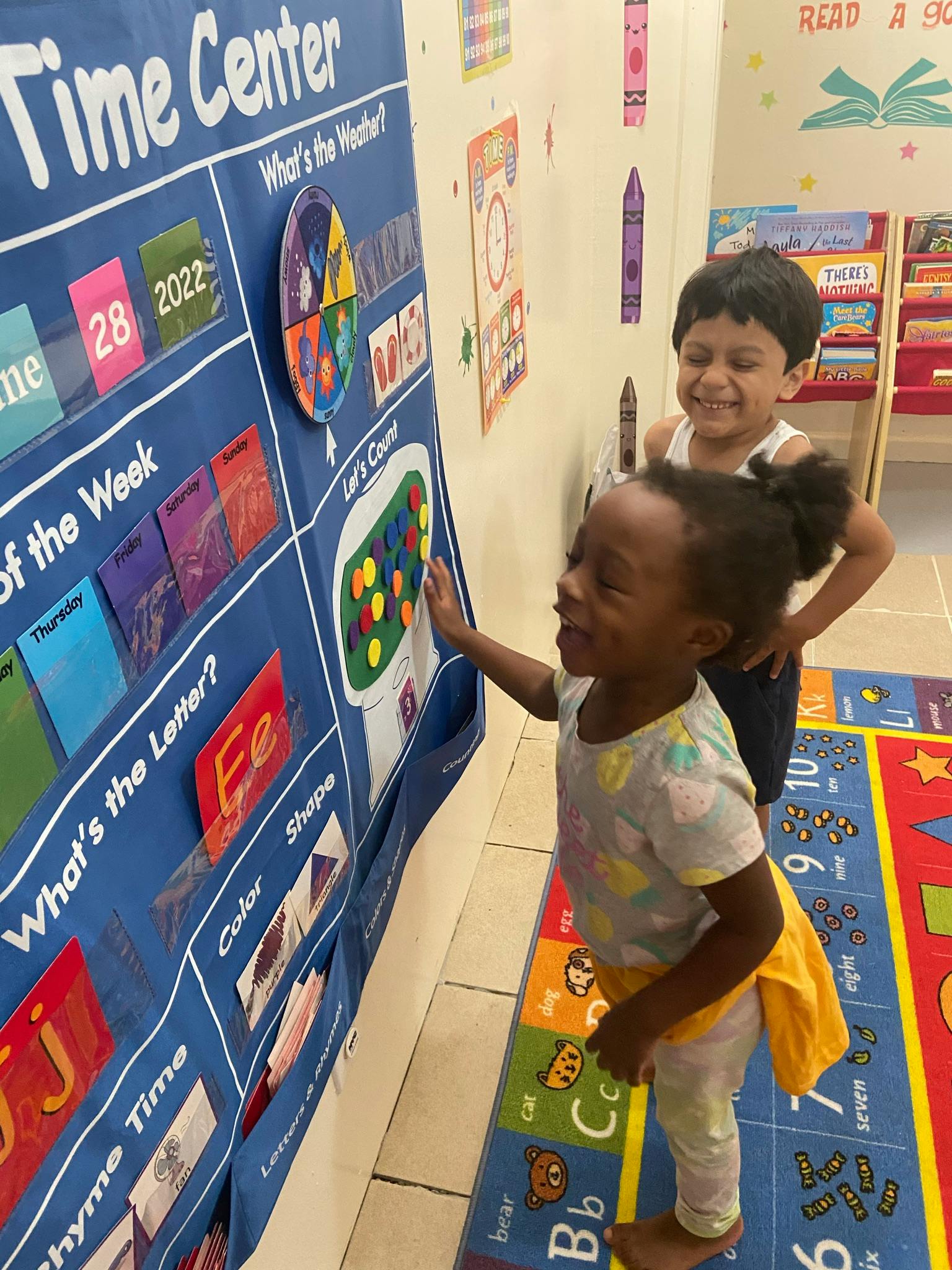 Two children interacting with a blue learning chart in a classroom