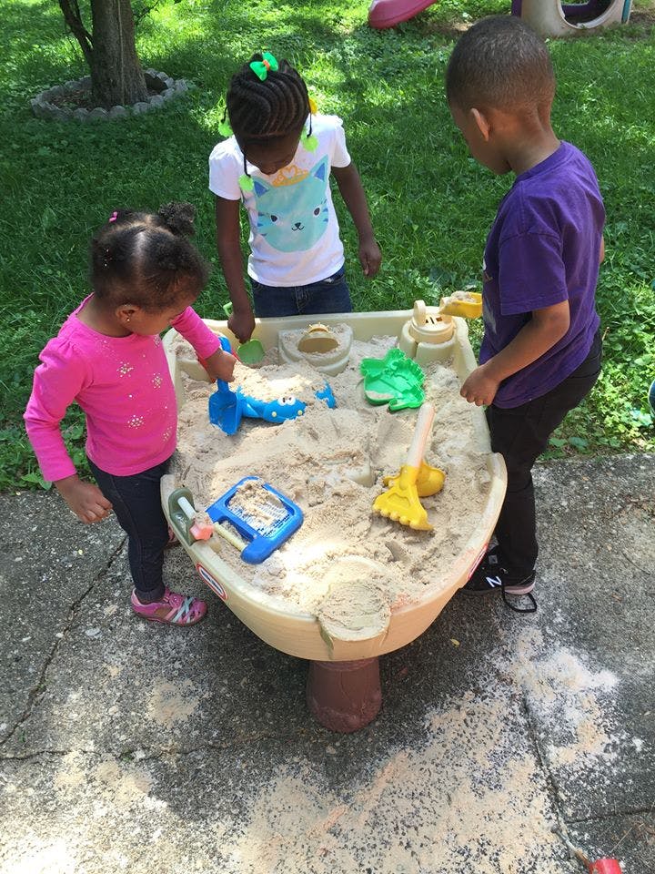 Three children playing in a sand table outdoors