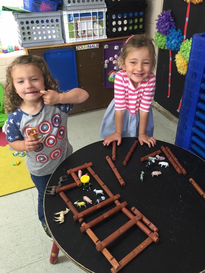 Two children playing with toy animals and wooden blocks on a table