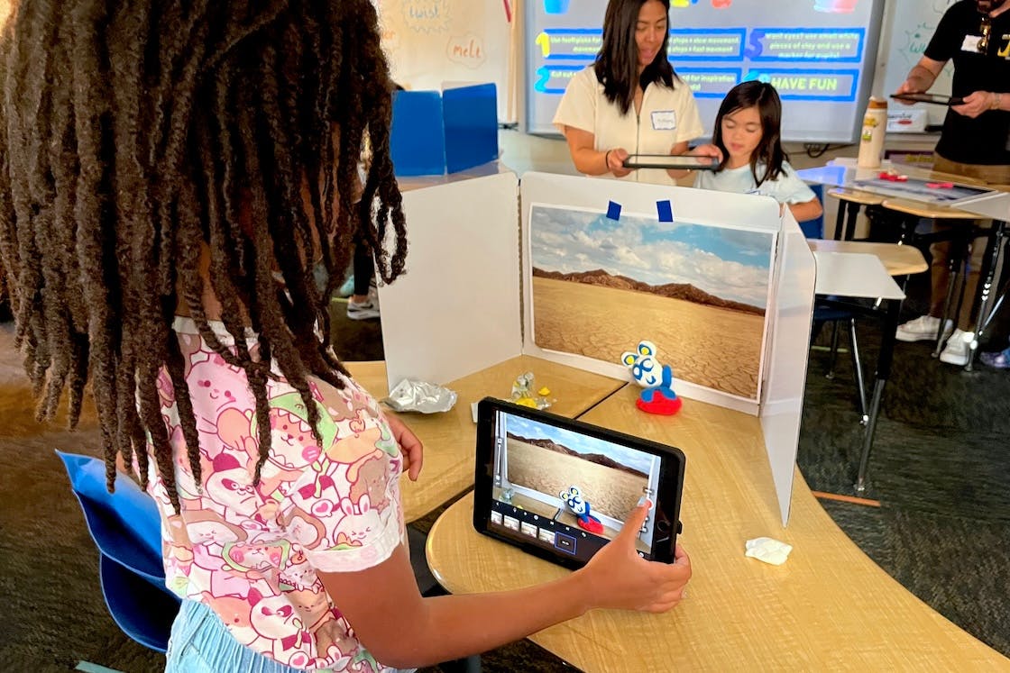 Child operating a tablet to photograph a clay figure against a desert background