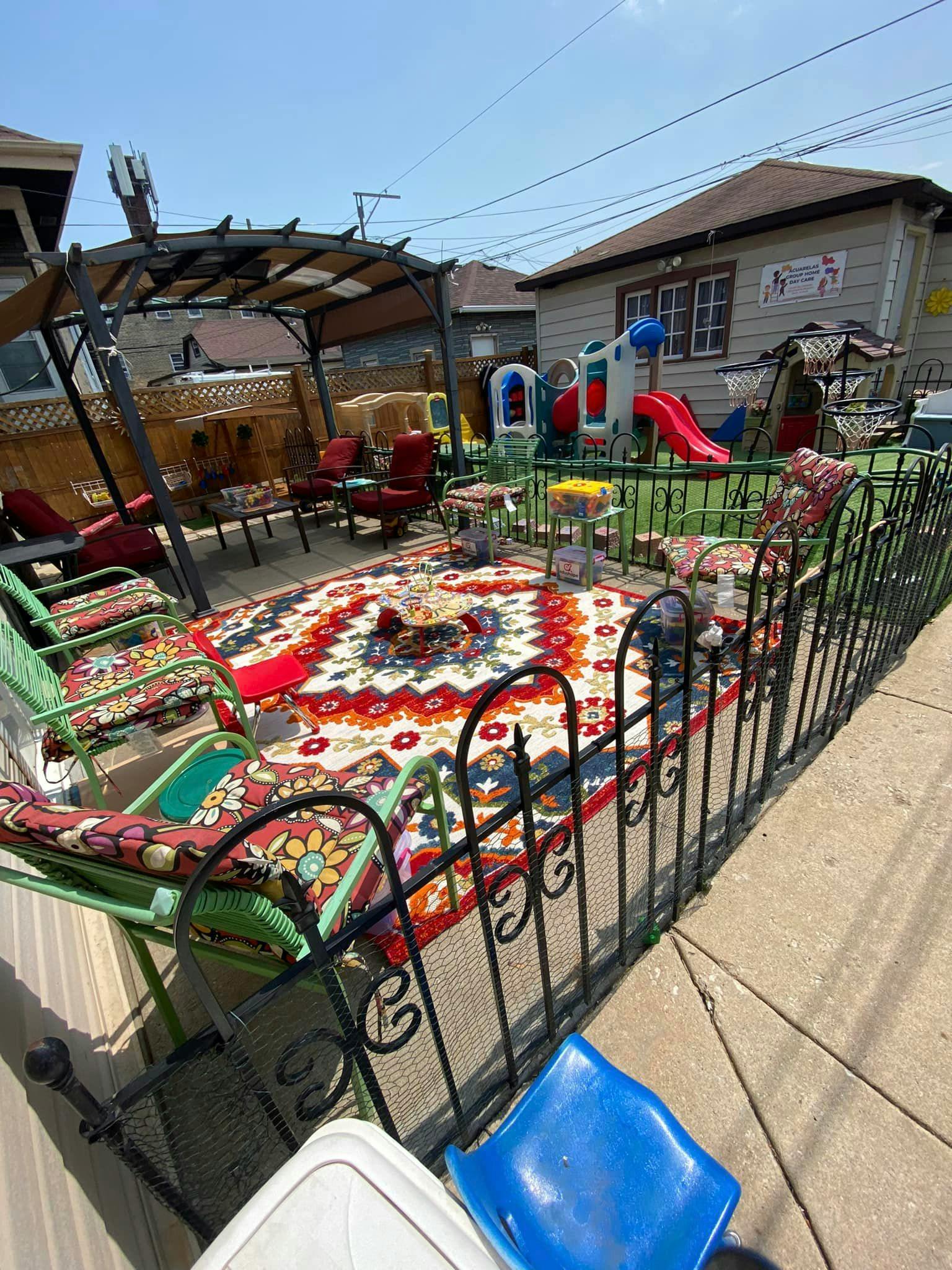 Outdoor patio with a patterned rug, chairs, and a play structure in the background