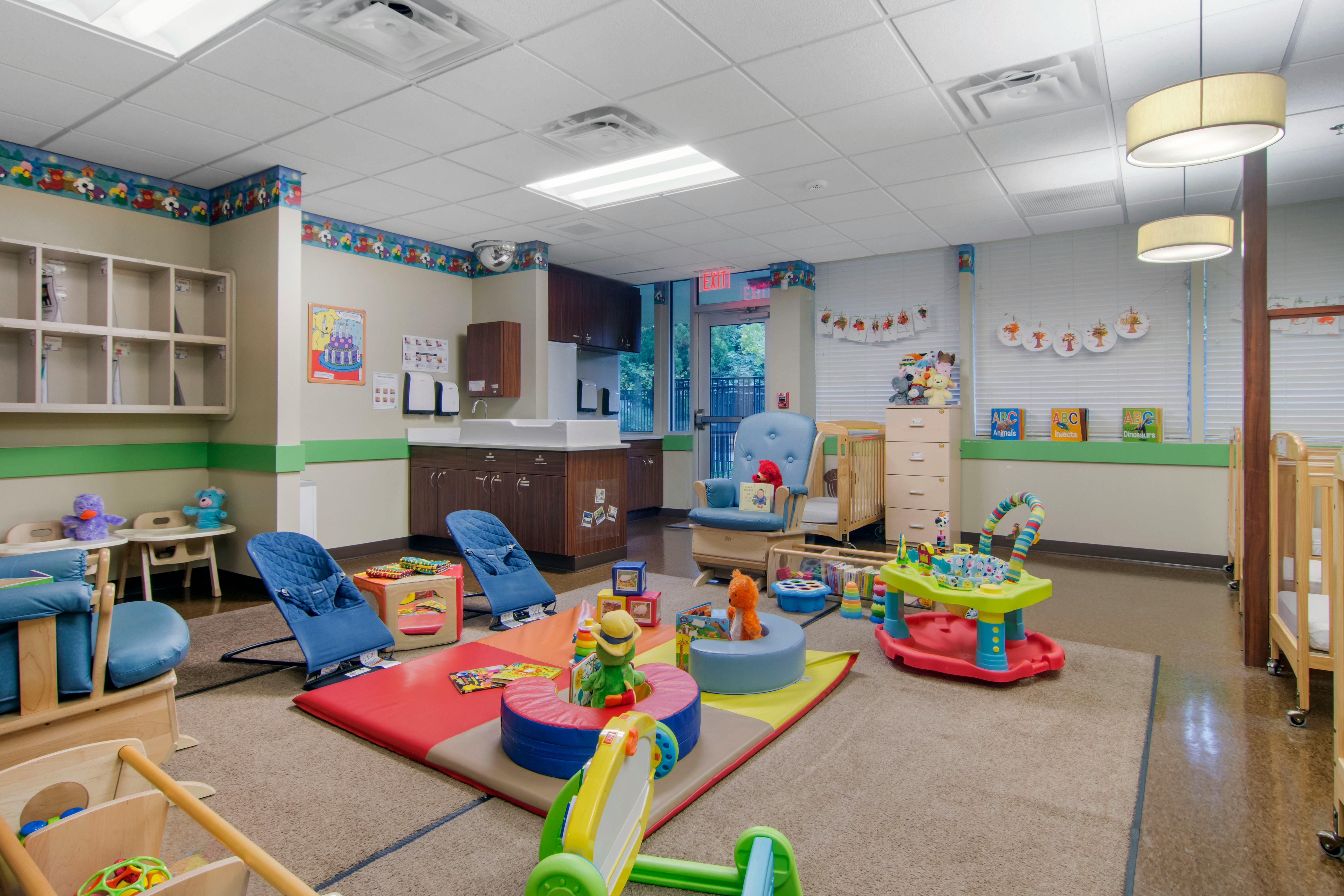A colorful childcare room with play mats, infant swings, and cribs