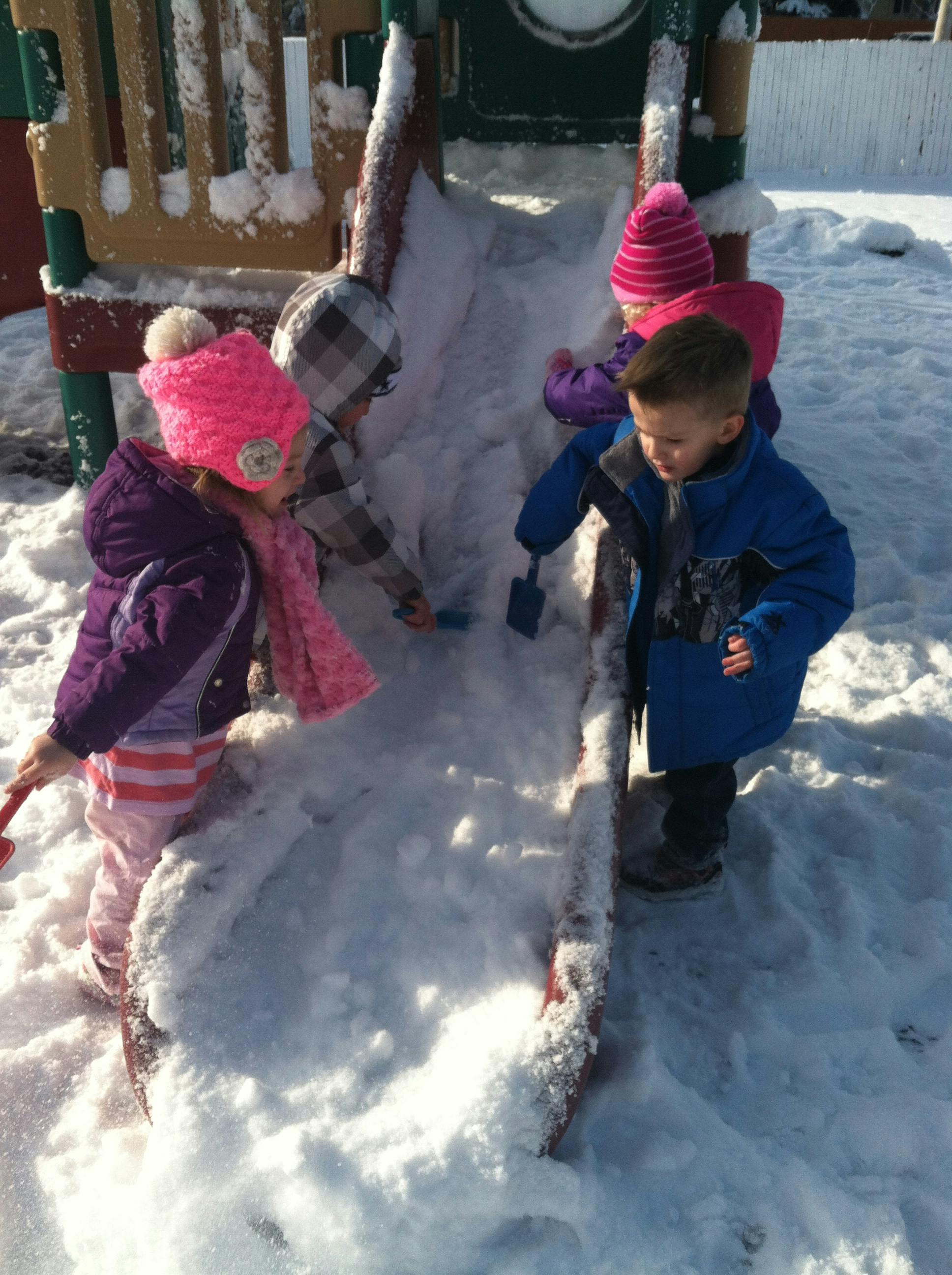 Children playing in snow on a playground slide
