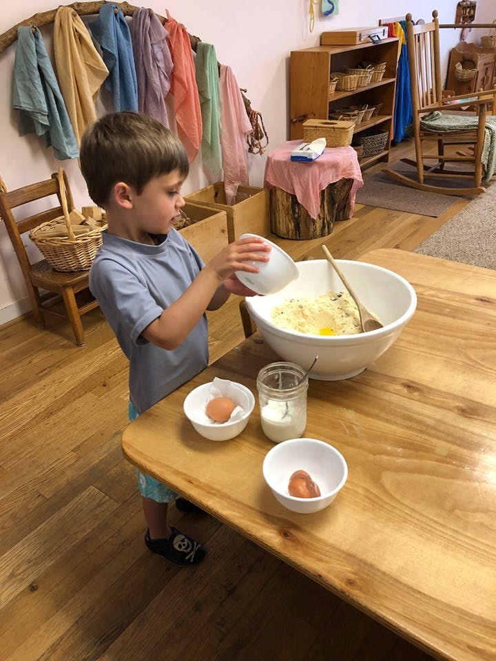 Child pouring ingredients from a small bowl into a large mixing bowl on a table