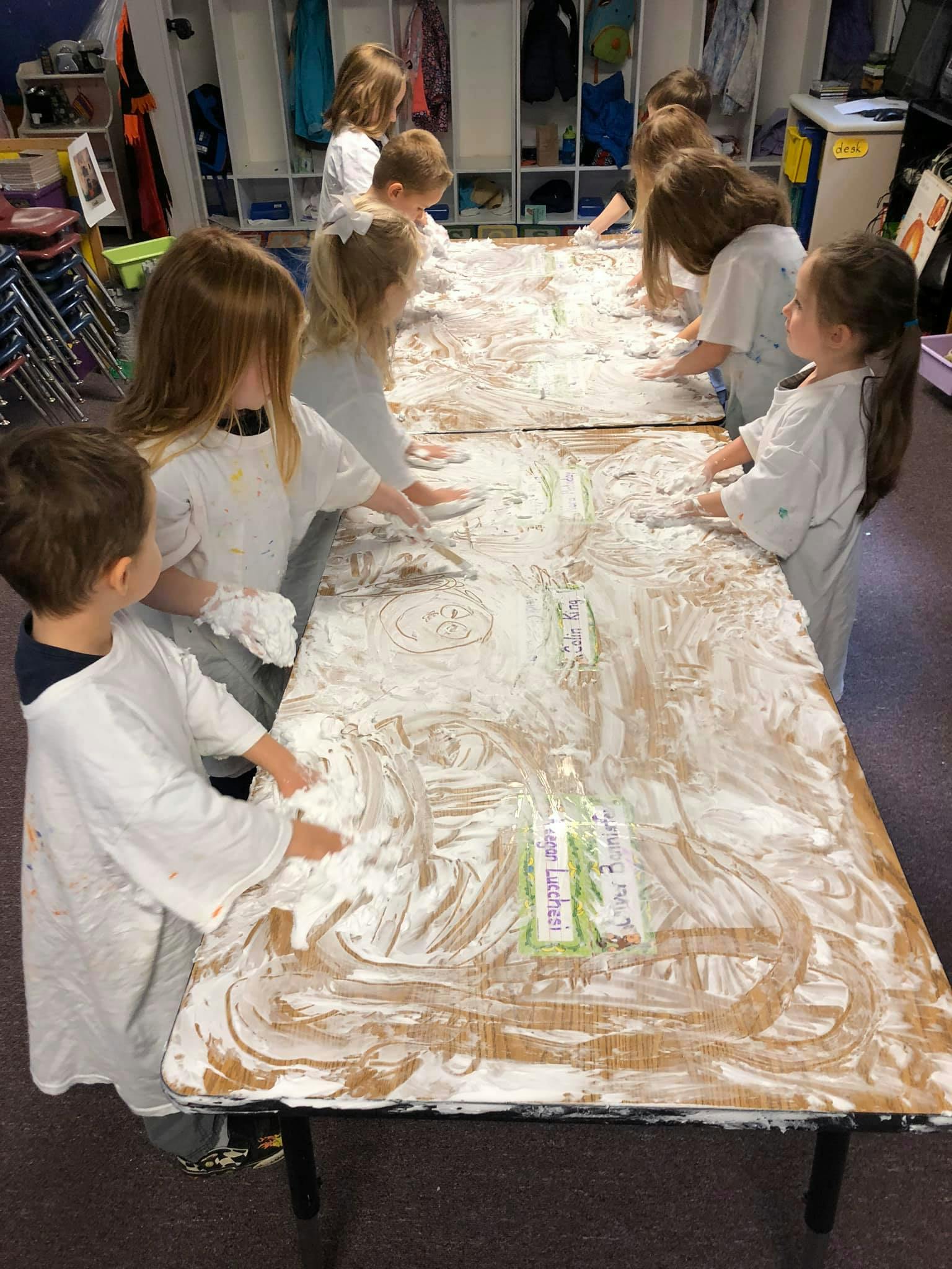 Children playing with shaving cream on a table in a classroom