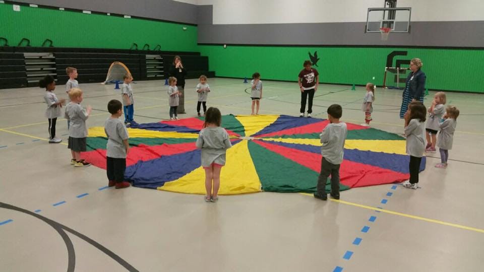 Children and adults standing around a colorful parachute in a gym