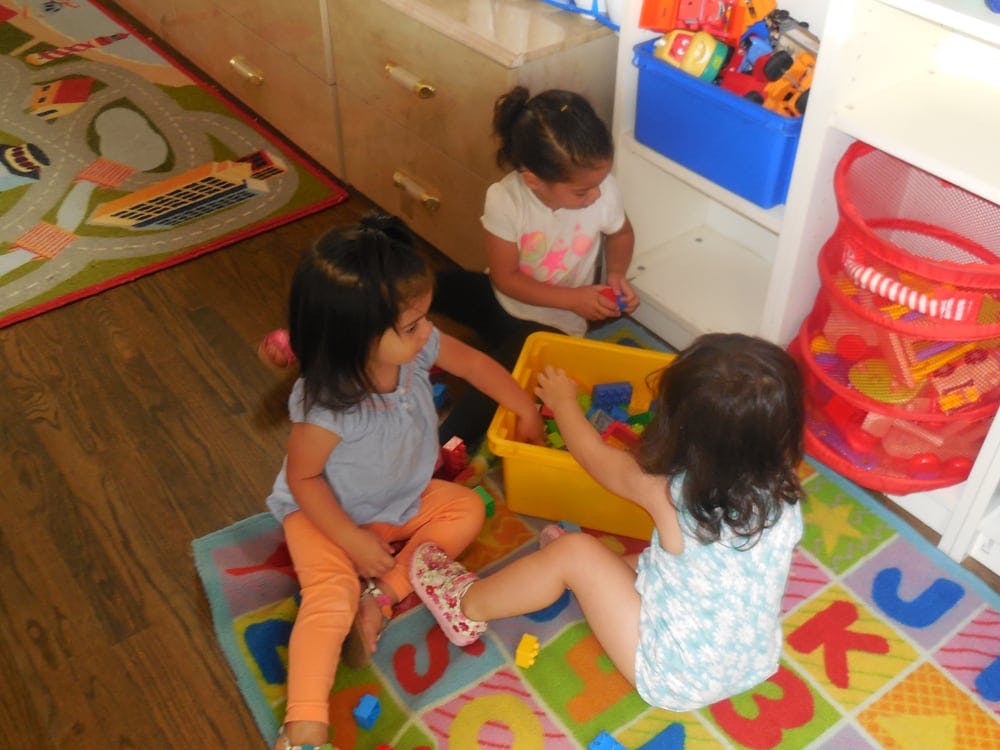 Three children playing with toys in a yellow bin on a colorful rug