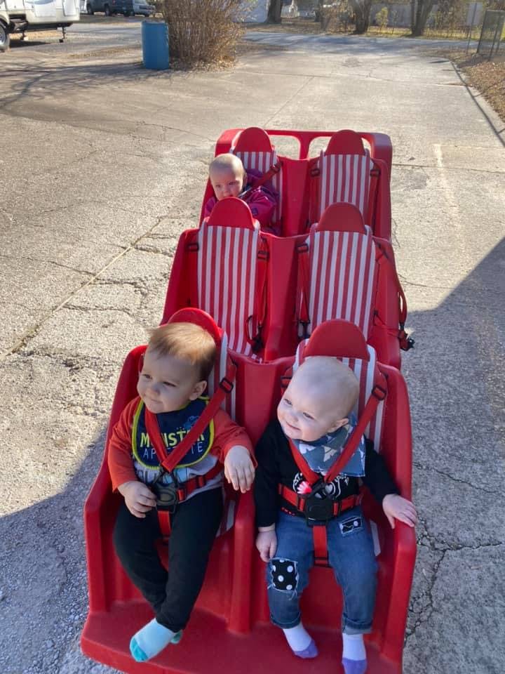 Three children in a red multi-seat stroller
