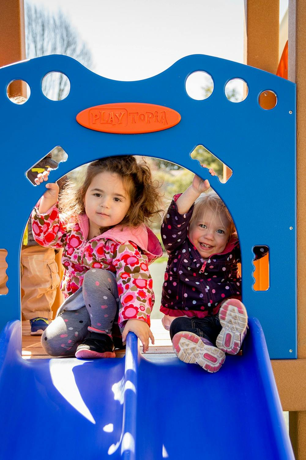 Two children at the top of a slide on a playground, one looking forward