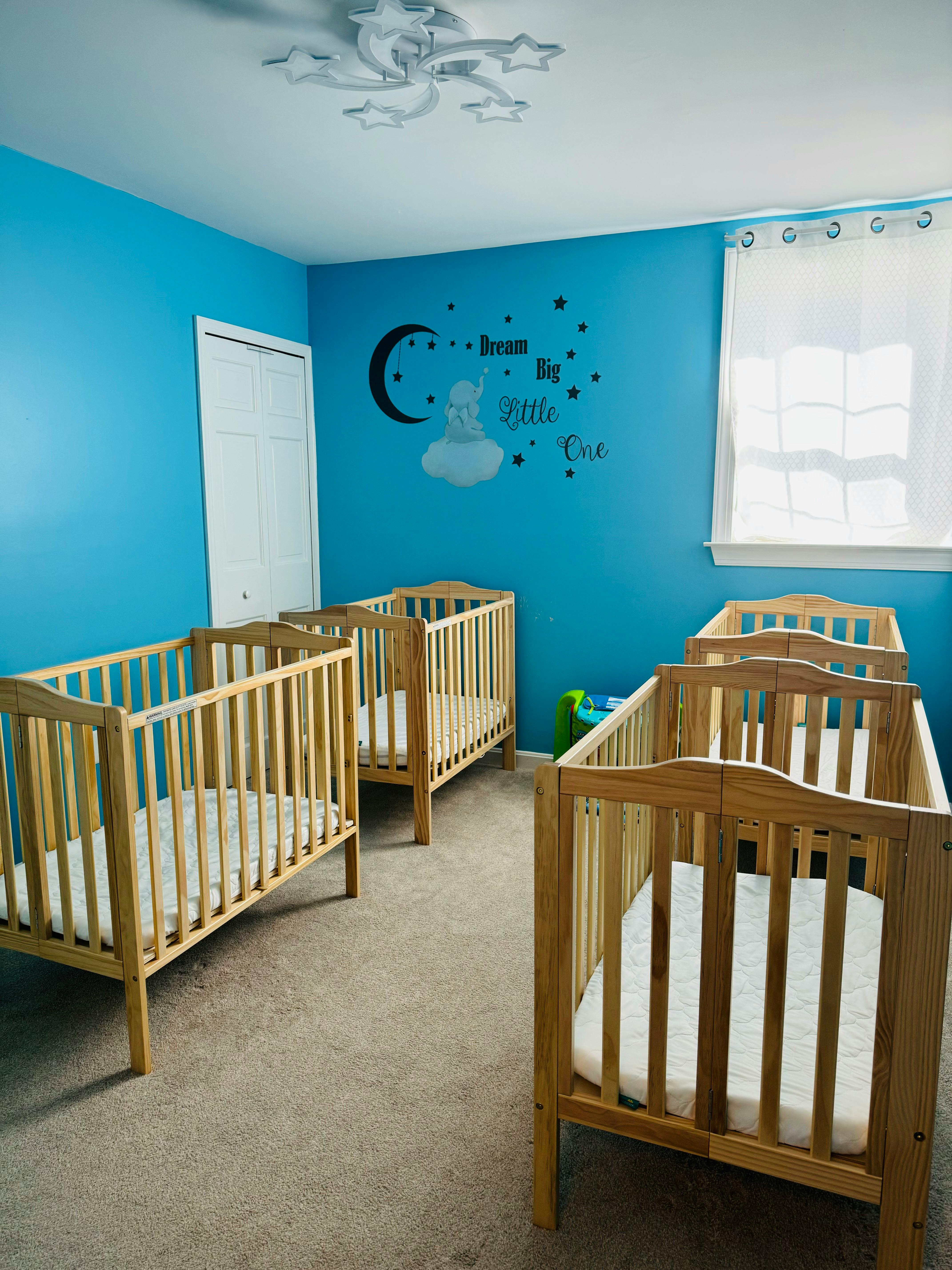 Multiple wooden cribs in a room with blue walls and a "Dream Big Little One" decal