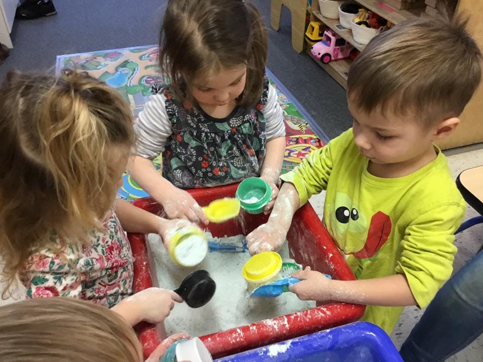 Three children playing with scoops and cups in a sensory bin