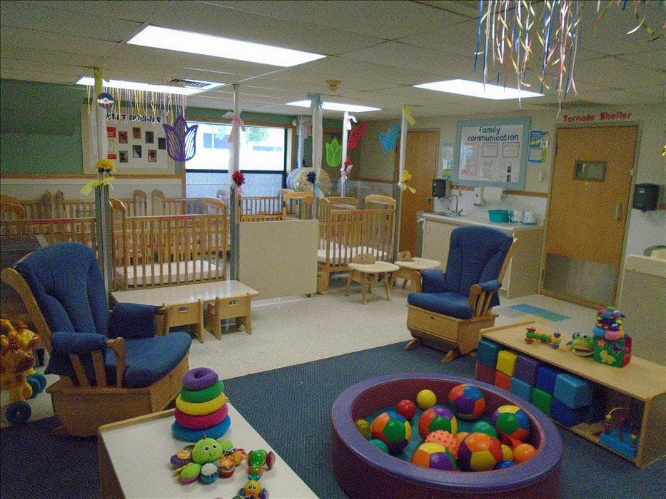 A colorful childcare classroom with cribs, rocking chairs, and toys