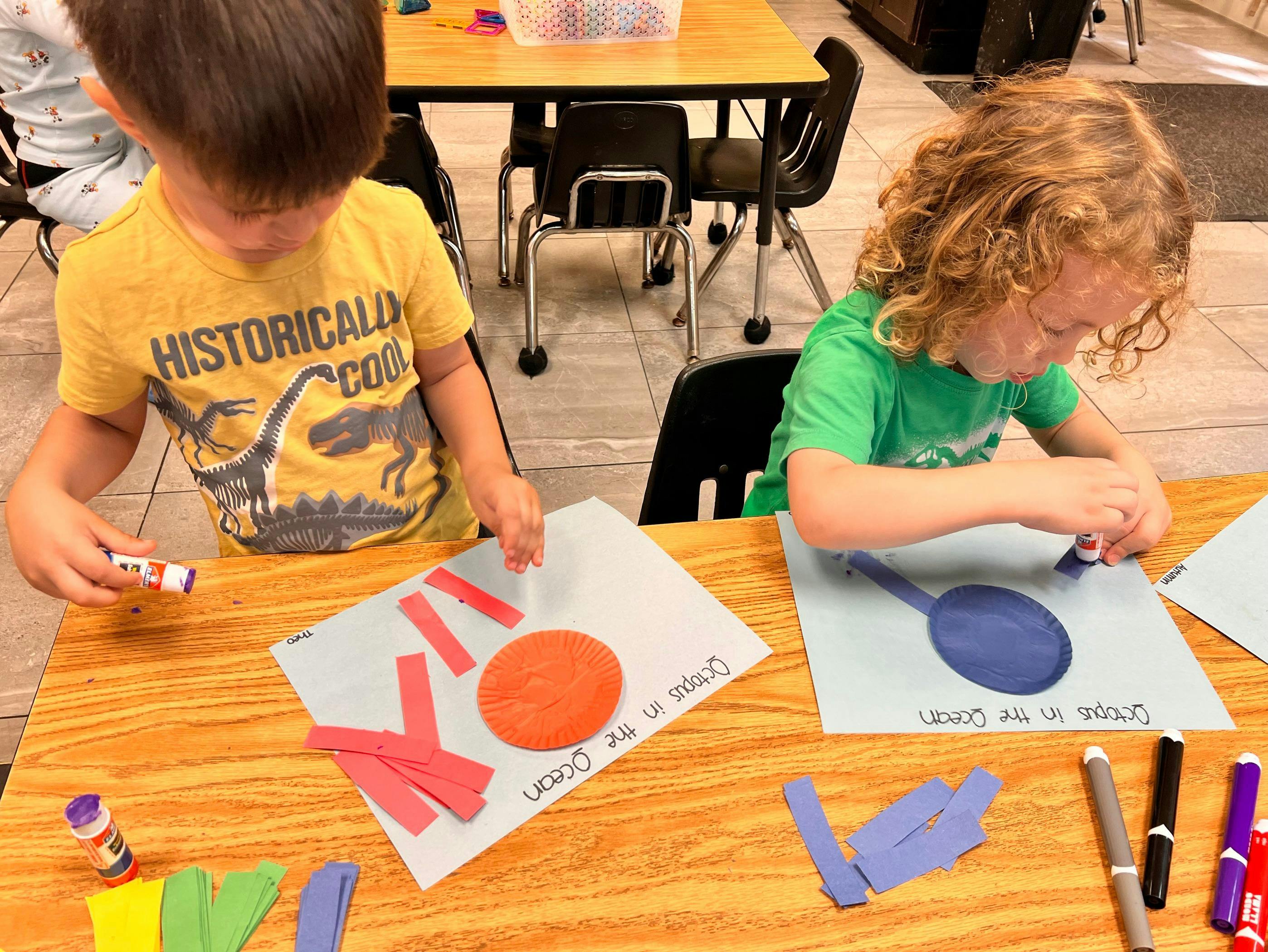 Two children gluing paper octopus crafts at a table