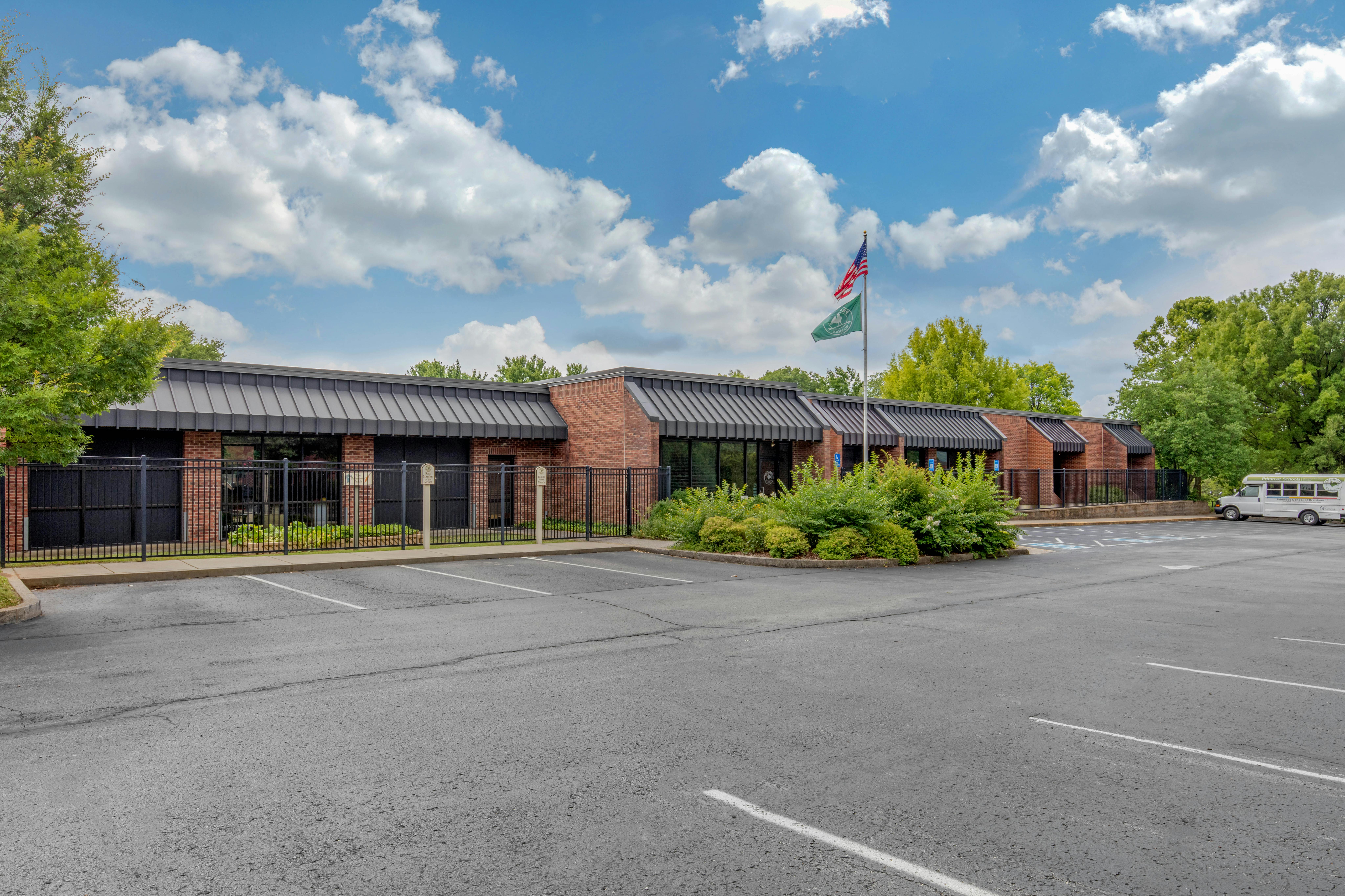 Brick building with black awnings, a parking lot, and a bus
