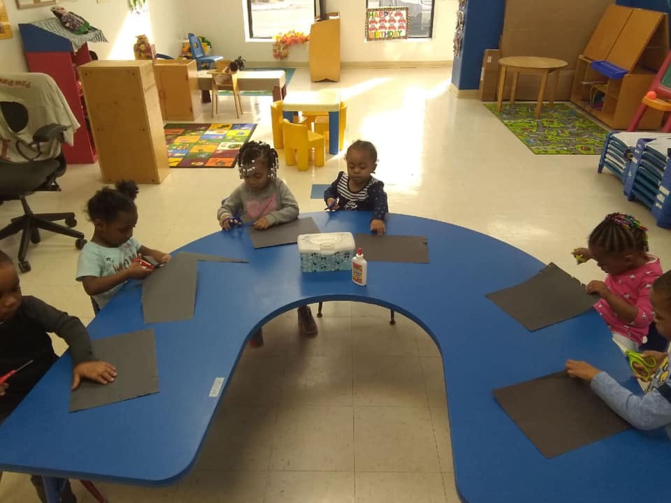 Children sitting at a blue table cutting paper