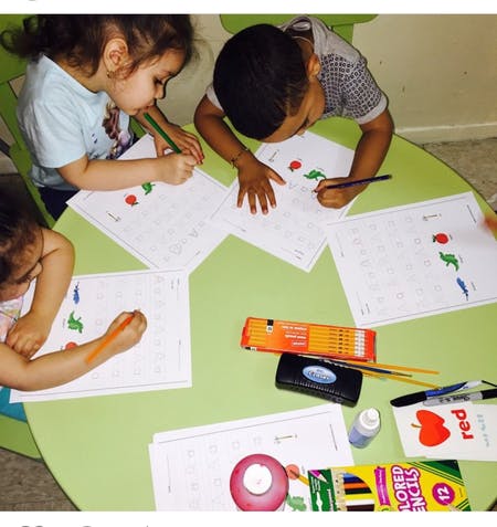 Three children drawing on papers at a green table