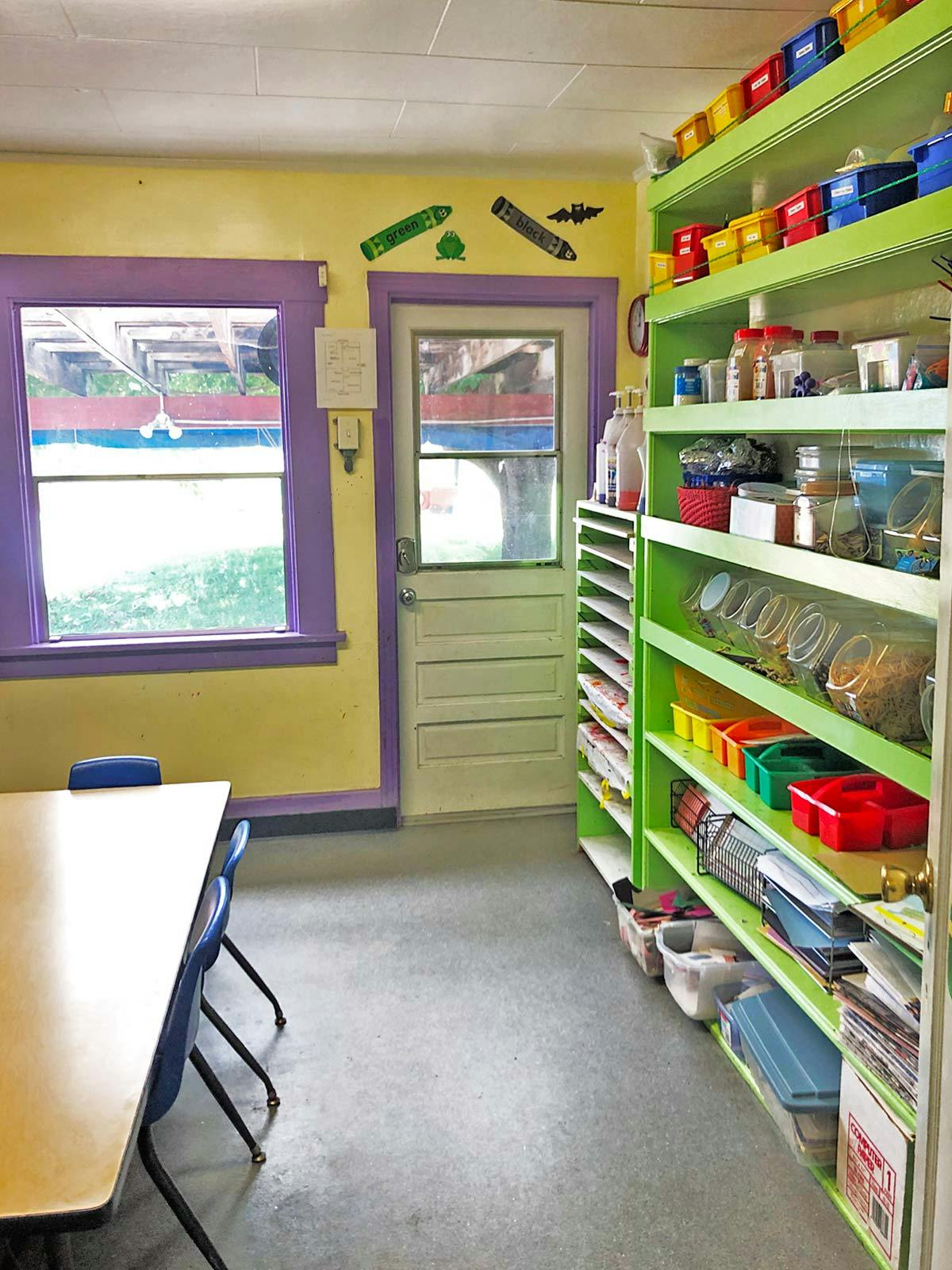 Classroom with a table and chairs, shelves with supplies, and a window