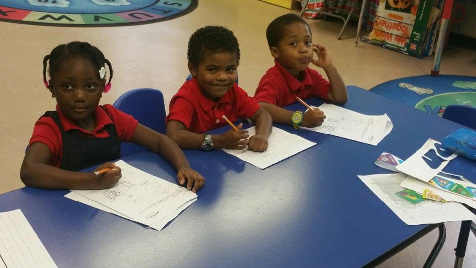 Three children sitting at a table with papers and pencils