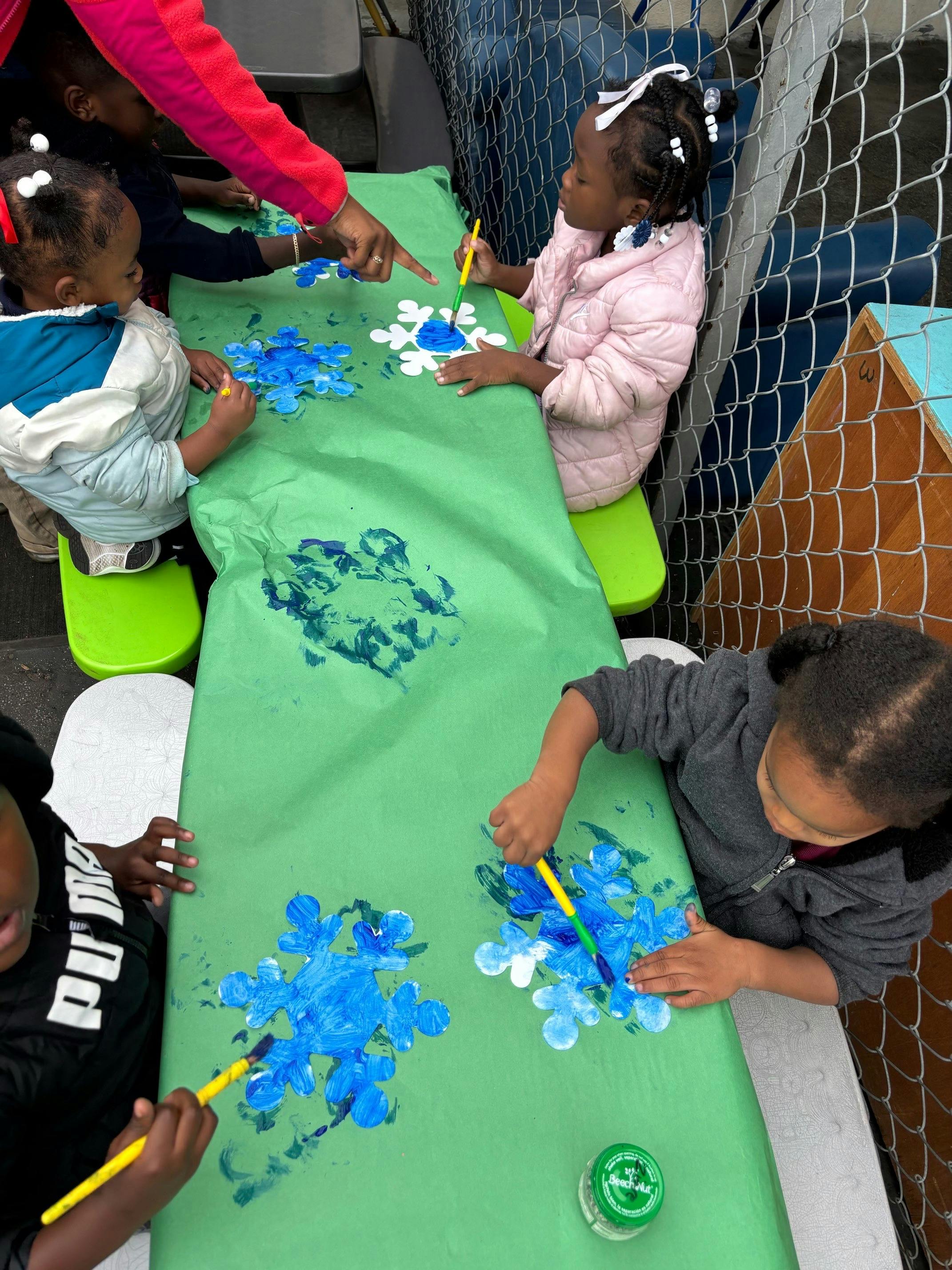 Children painting blue and white shapes on a green surface