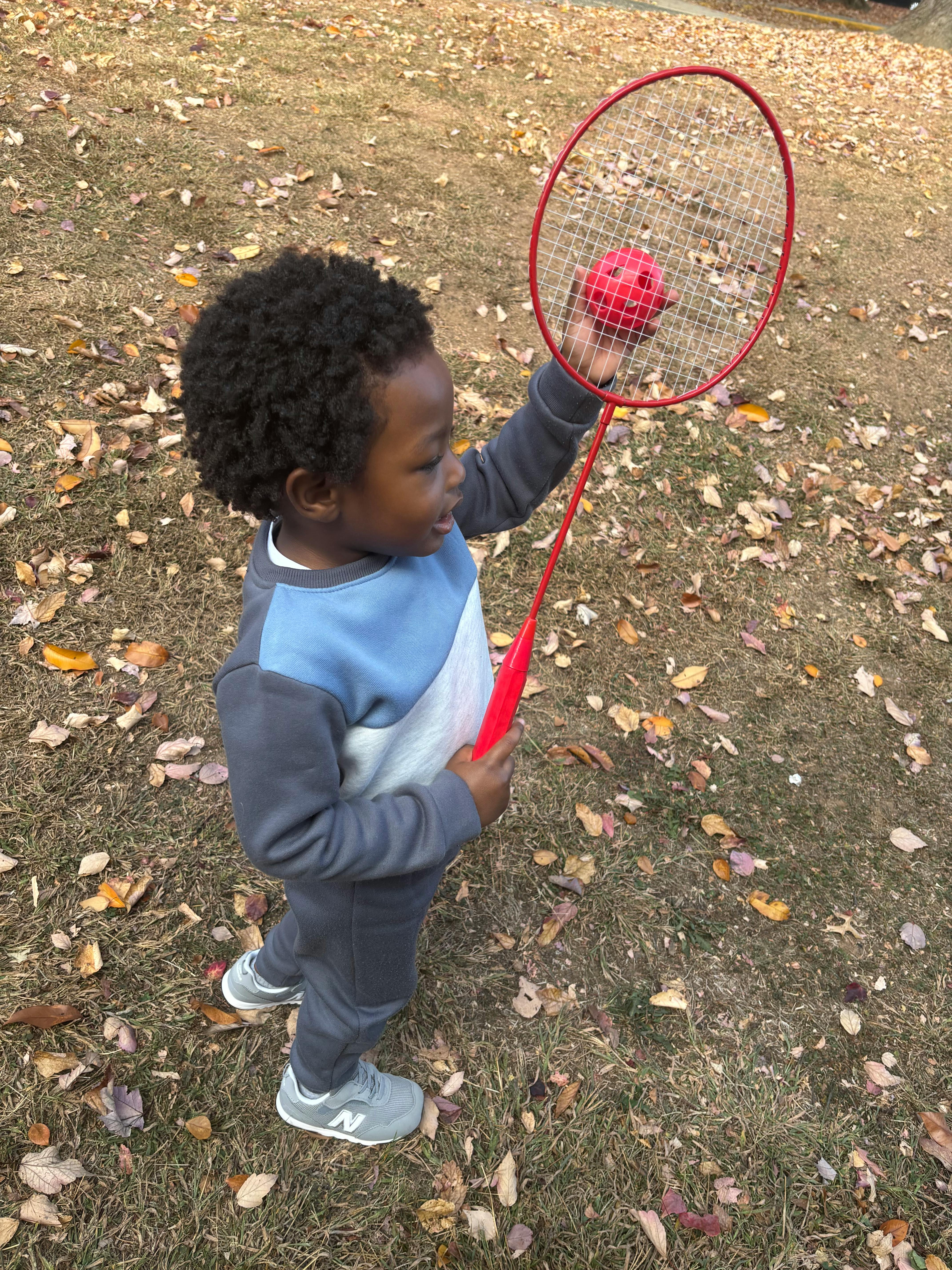 Child holding a red badminton racket with a red ball on the strings