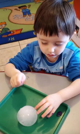 Child playing with a white ball on a green tray