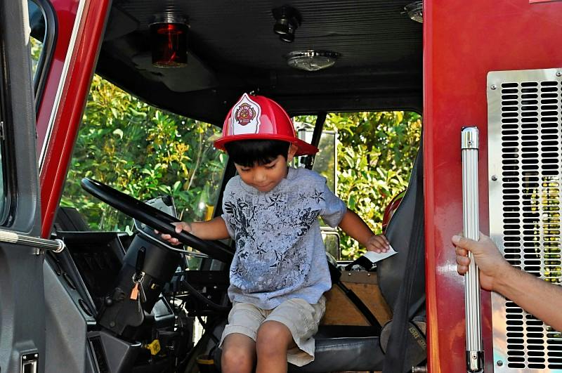 Child in a red firefighter helmet sitting in a fire truck cab