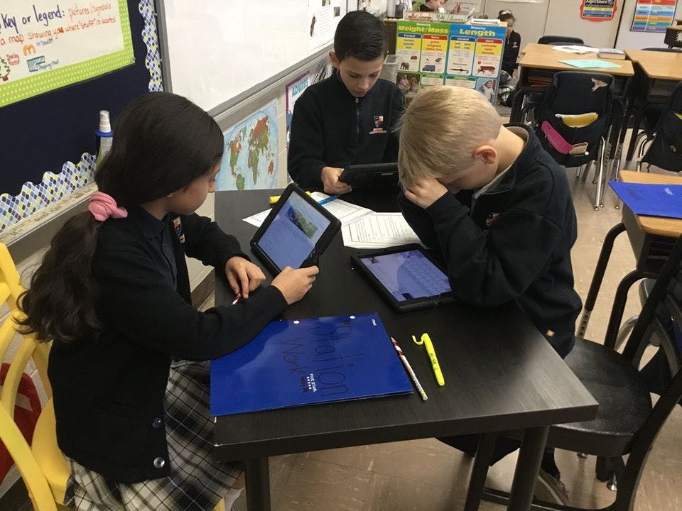 Three children using tablets at desks in a classroom