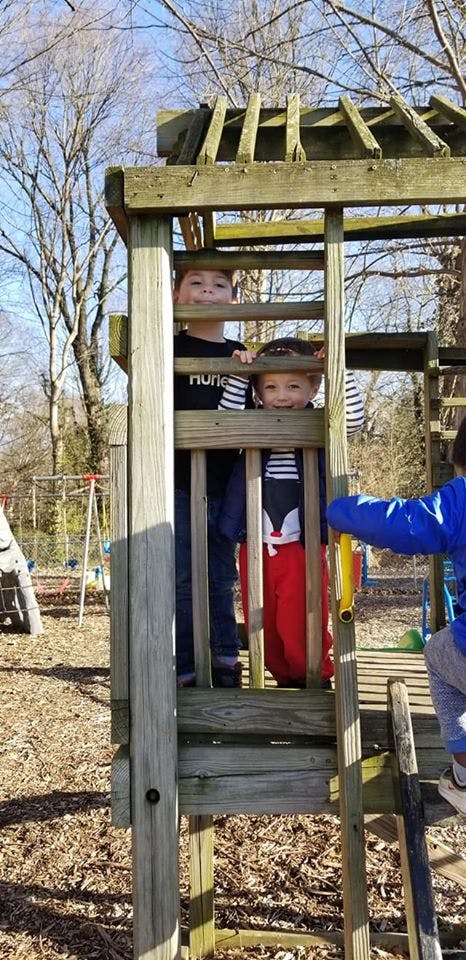 Two children looking out from a wooden play structure