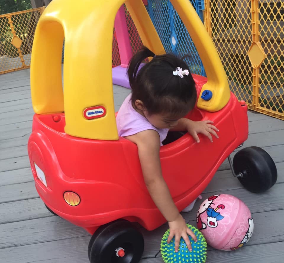 Child in a toy car reaching for a ball