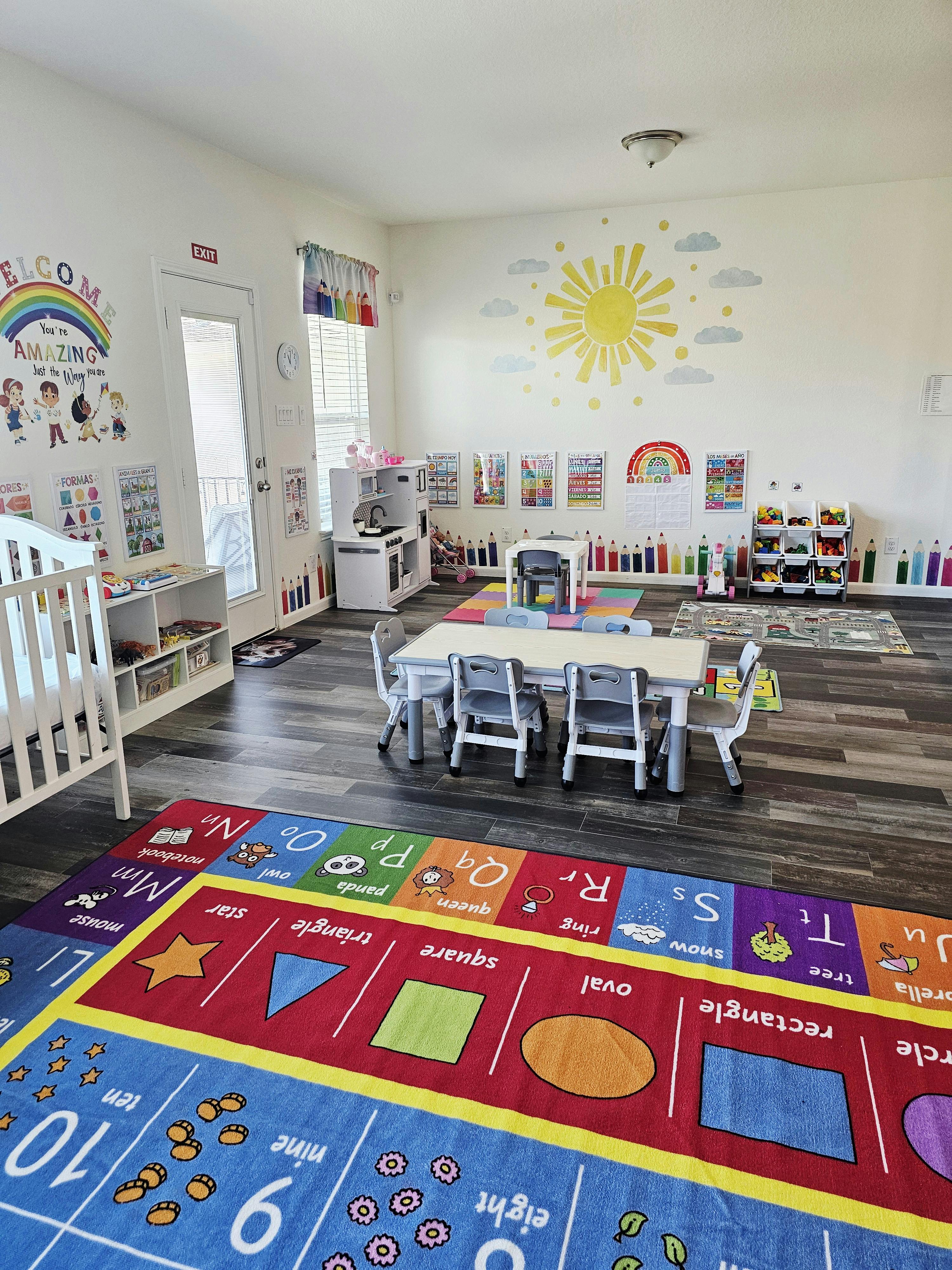 A brightly decorated classroom with a large colorful rug, tables, and chairs