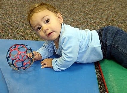Child on stomach reaching for a toy ball