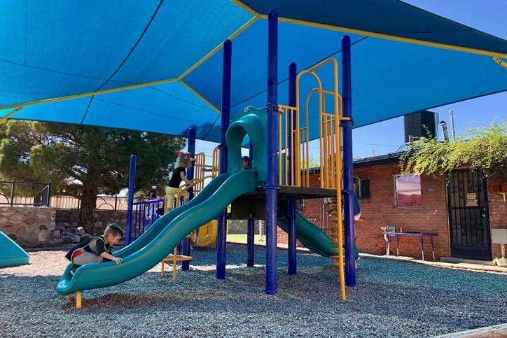 Child on a playground slide under a blue shade structure