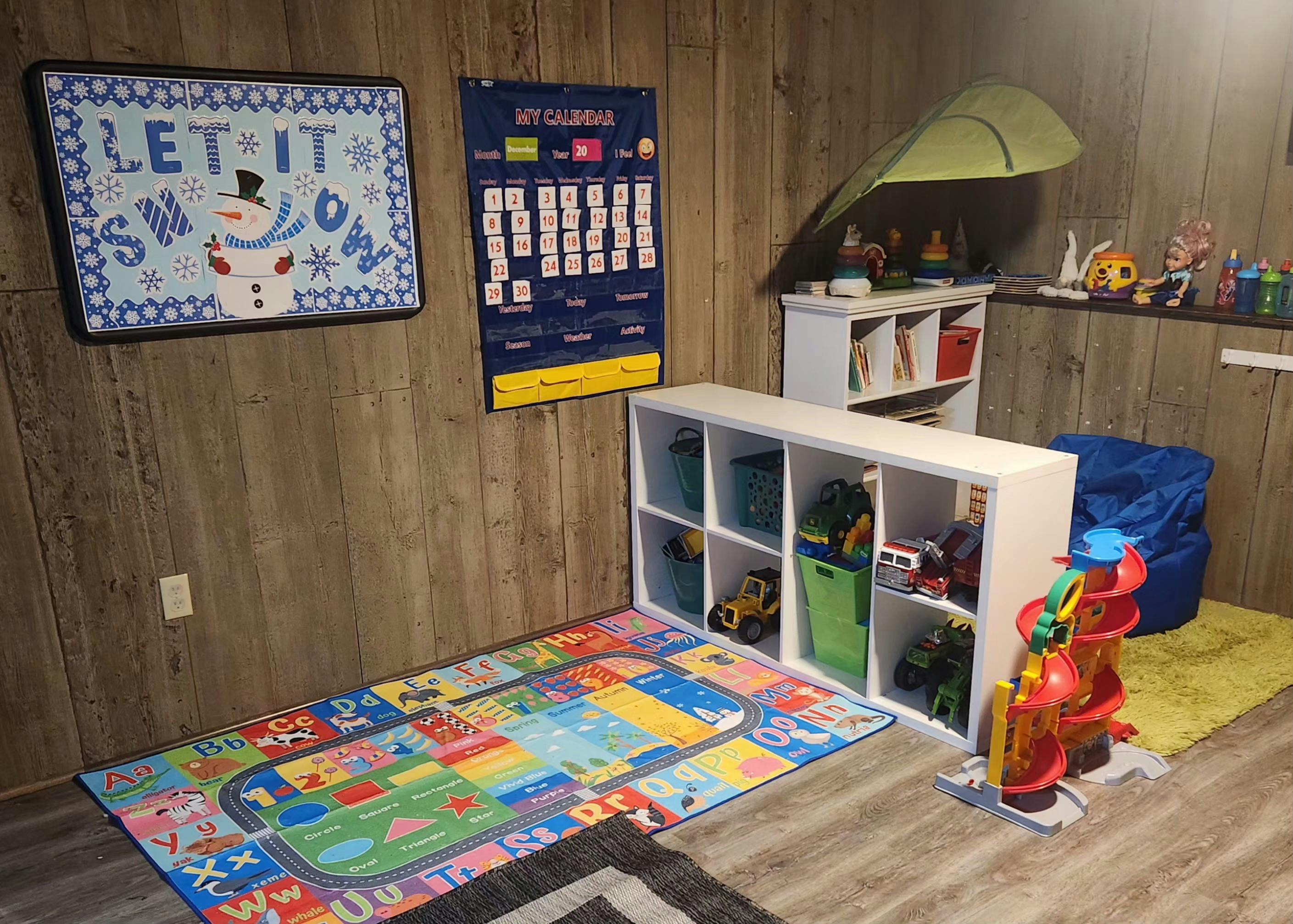 Child's play area with a winter sign, calendar, toy shelves, and playmat