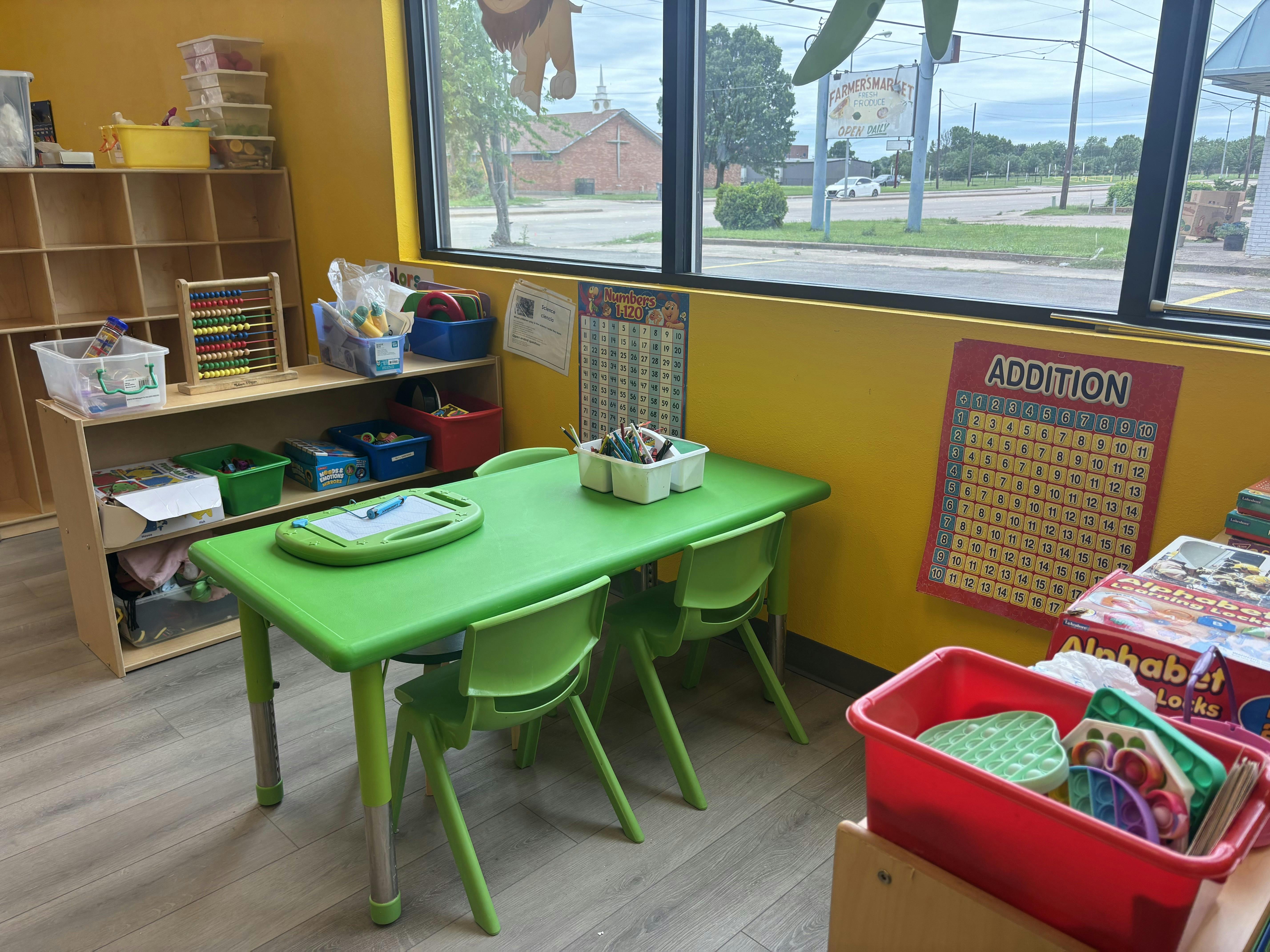Classroom area with a green table, small chairs, and educational wall charts