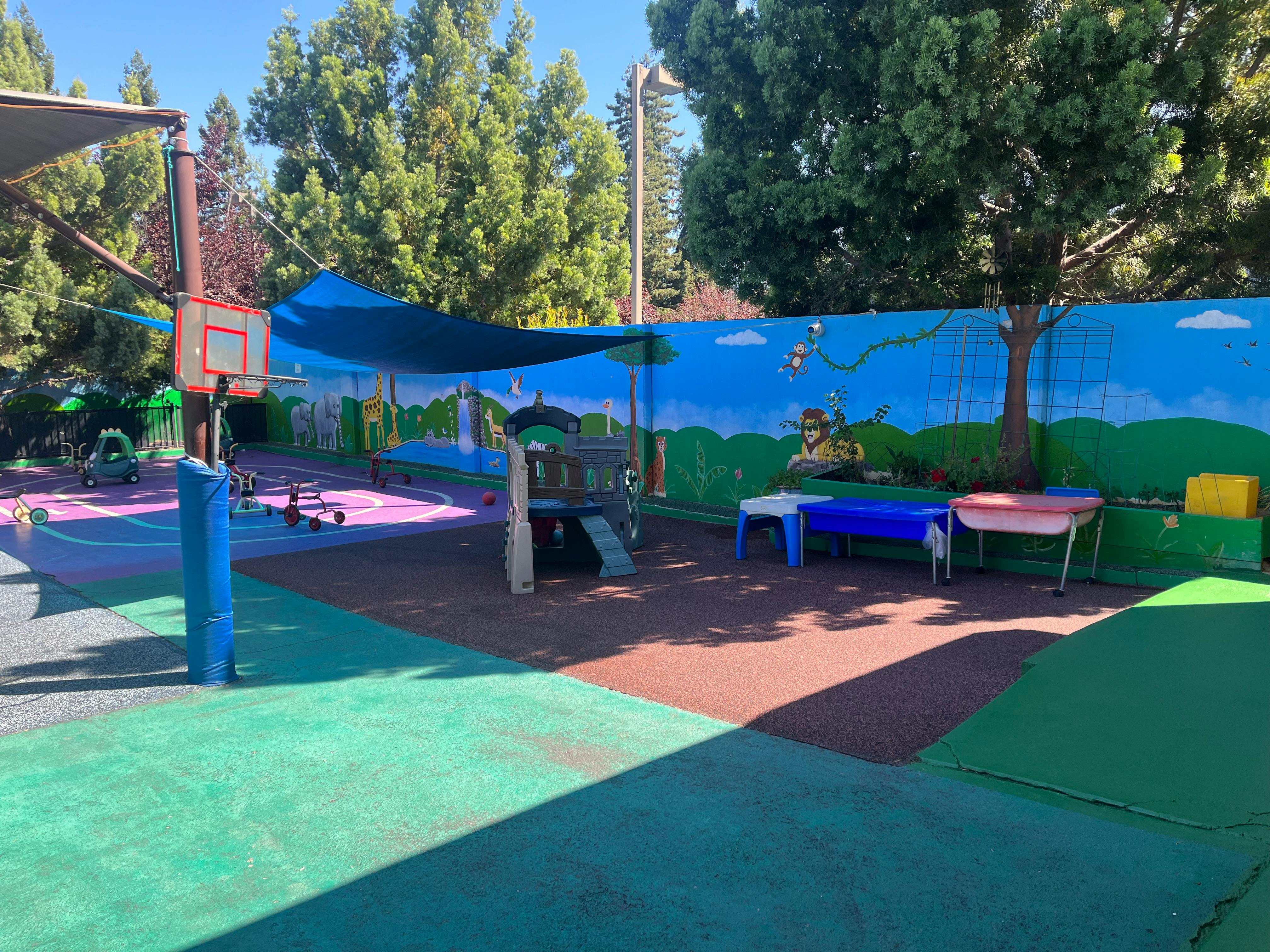 Outdoor playground with basketball hoop, slide, and painted fence