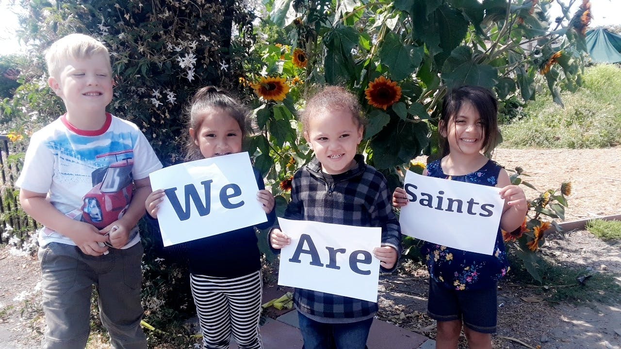 Four children holding signs that read "We Are Saints"