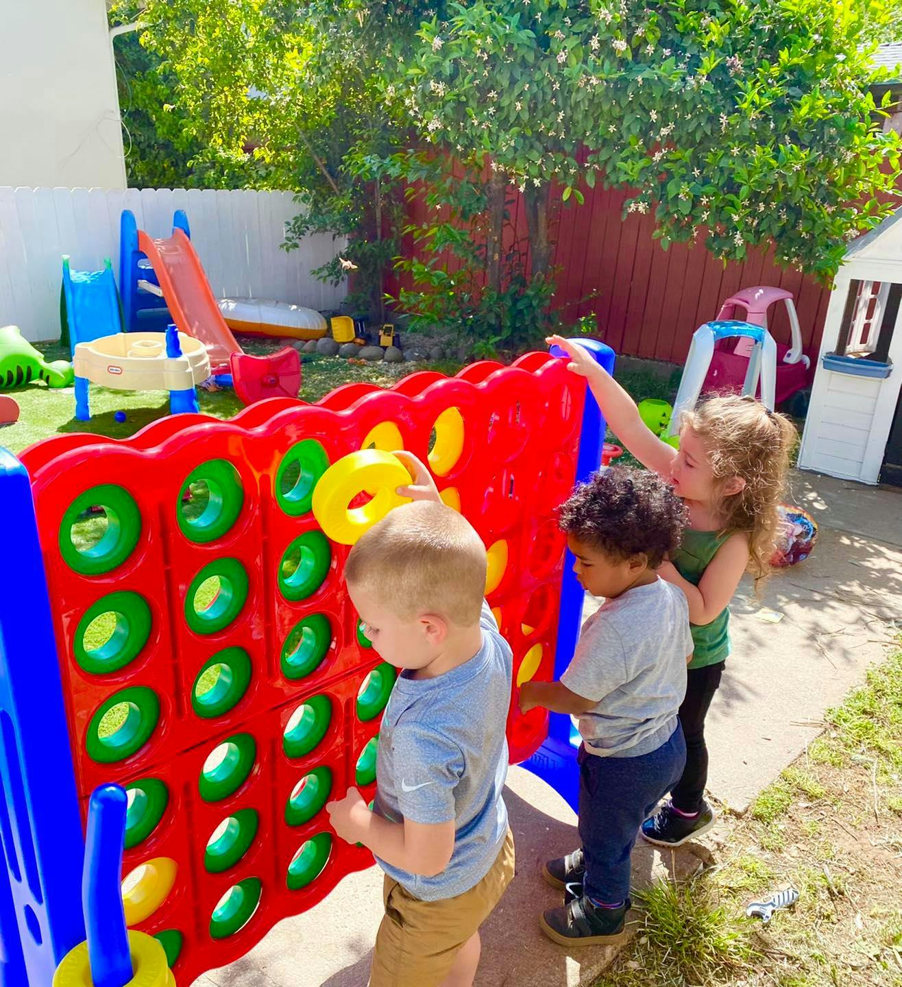 Three children playing with a large Connect 4 game outdoors