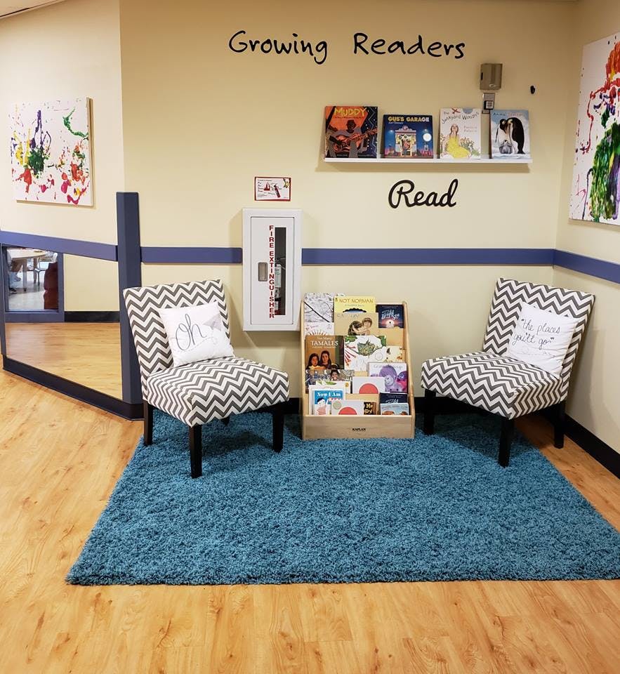 Two chairs and a book display on a blue rug with "Growing Readers" on the wall