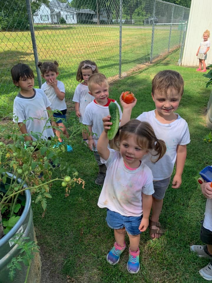 Children holding up a cucumber and a tomato in a garden