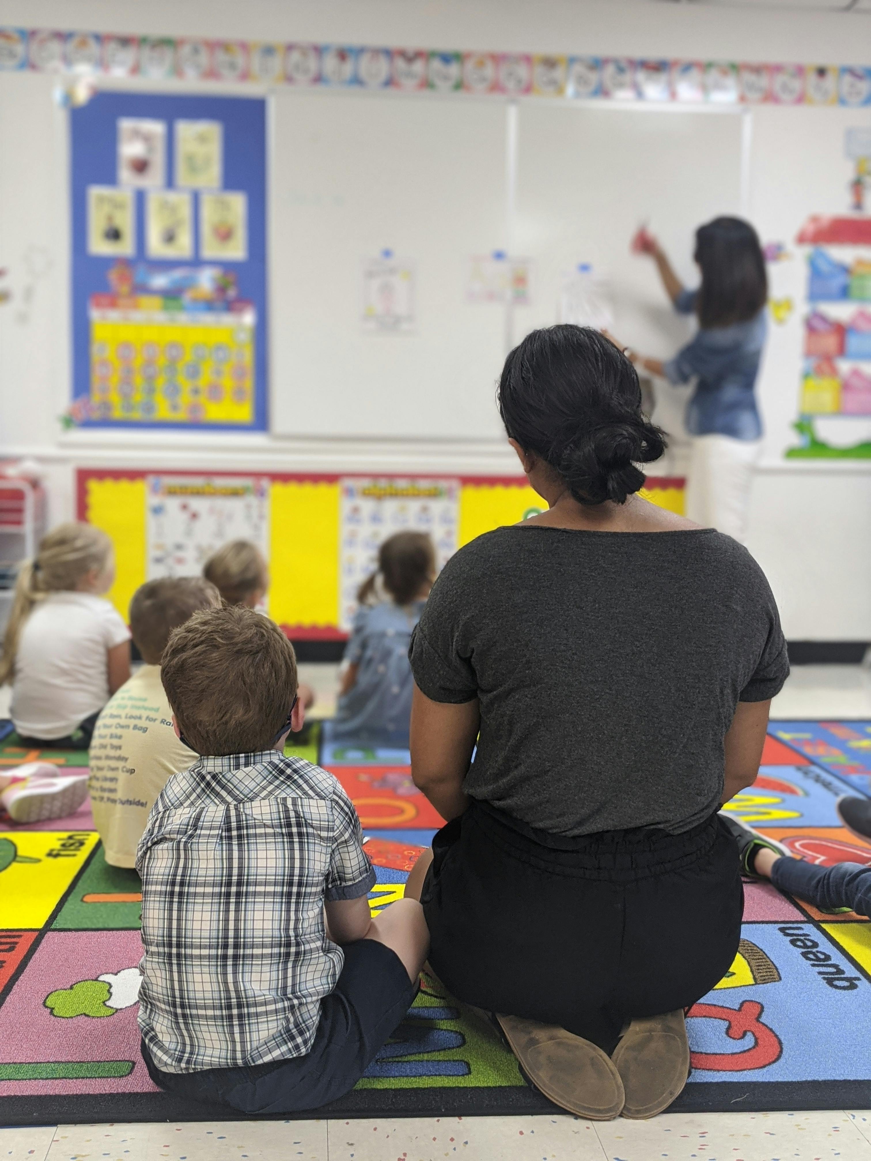 Adult and children sitting on a colorful rug in a classroom
