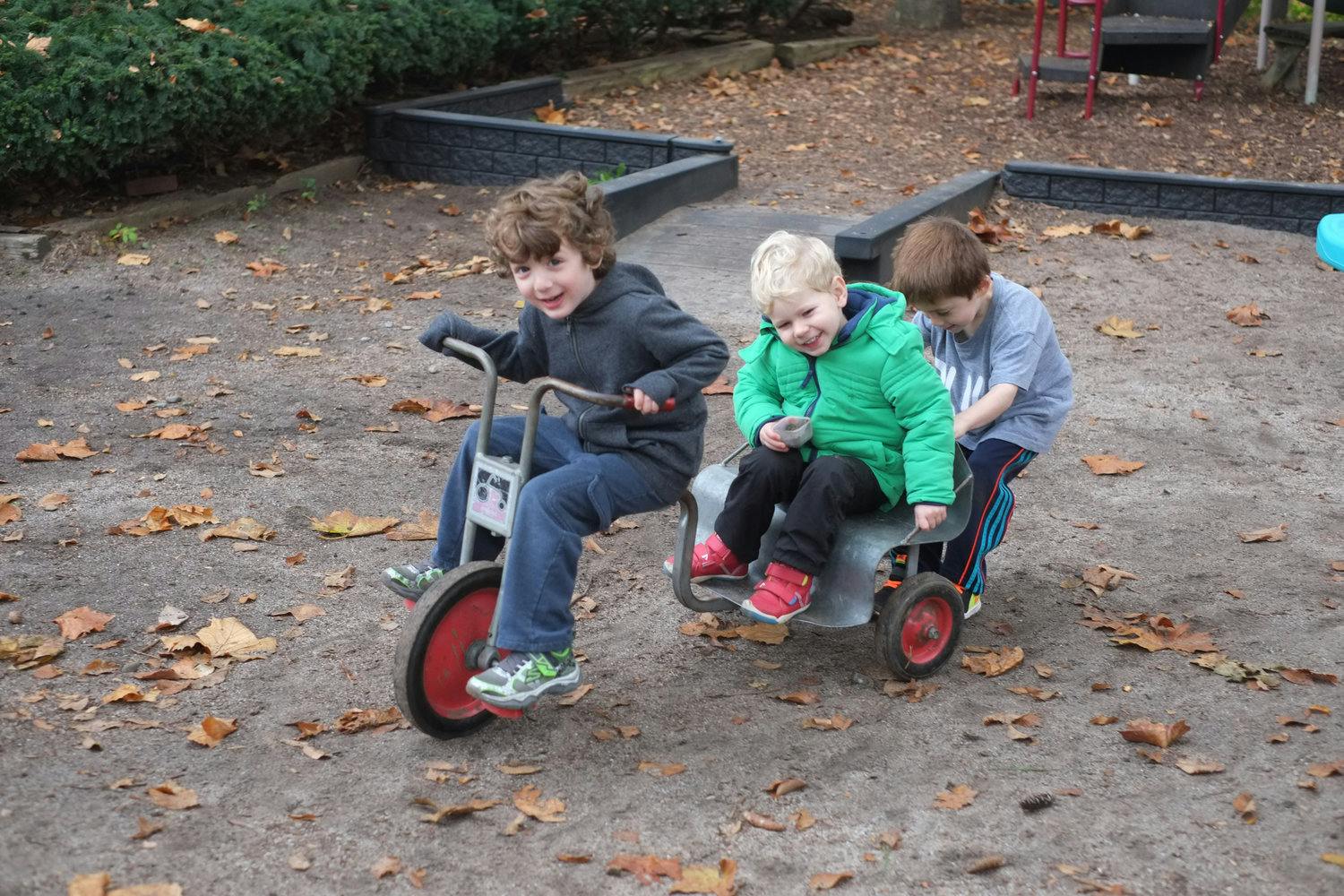 Three children playing on a tricycle with a wagon attachment