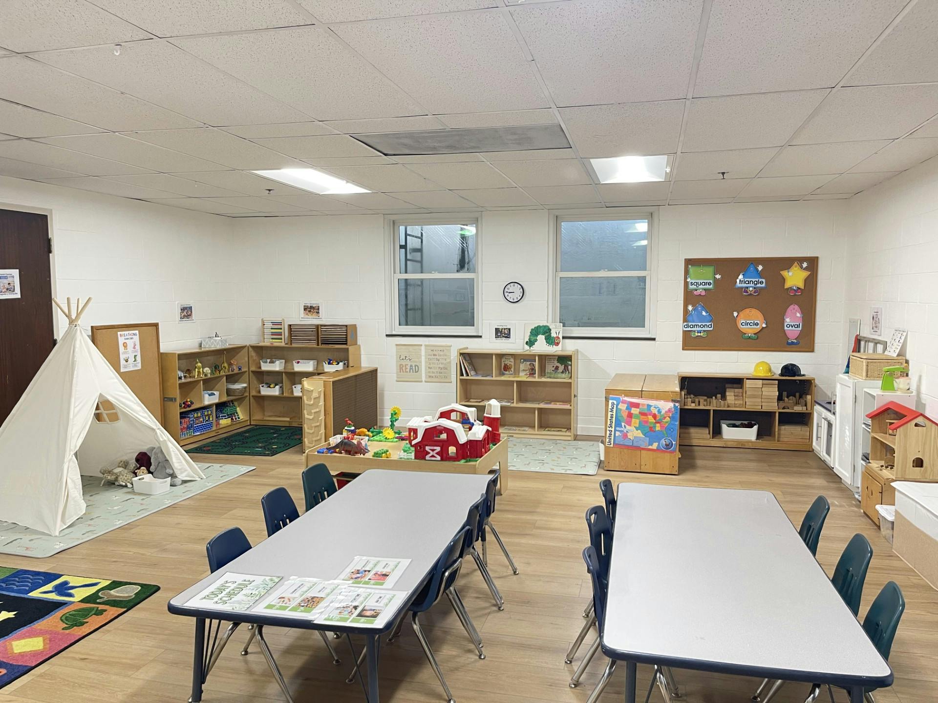 Classroom interior featuring tables, chairs, a toy tent, and educational decor