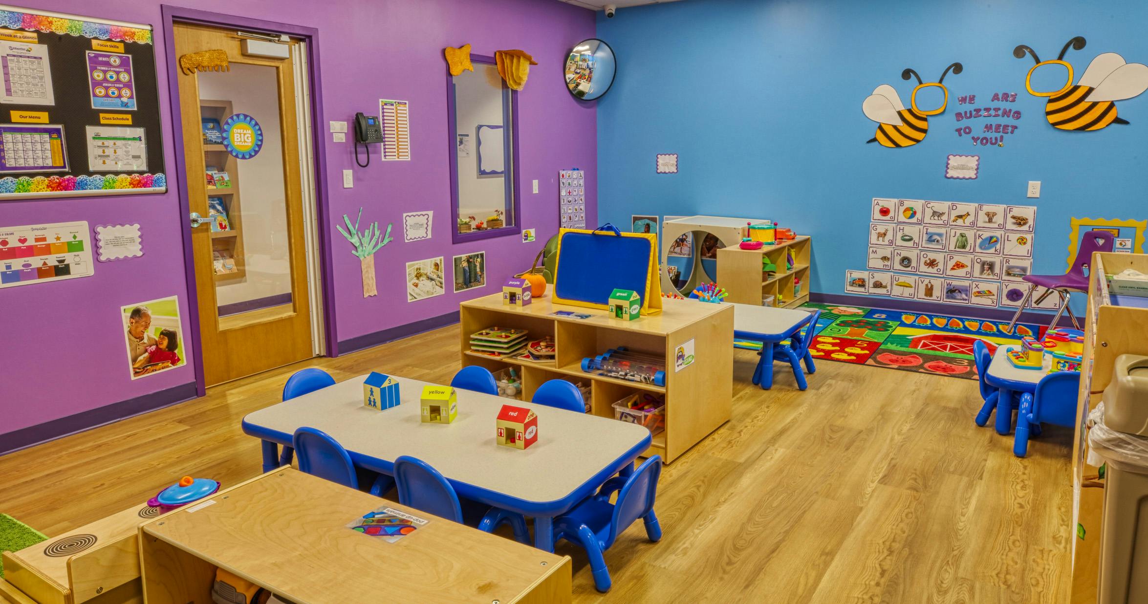 Colorful preschool classroom with small tables and chairs, shelves with toys