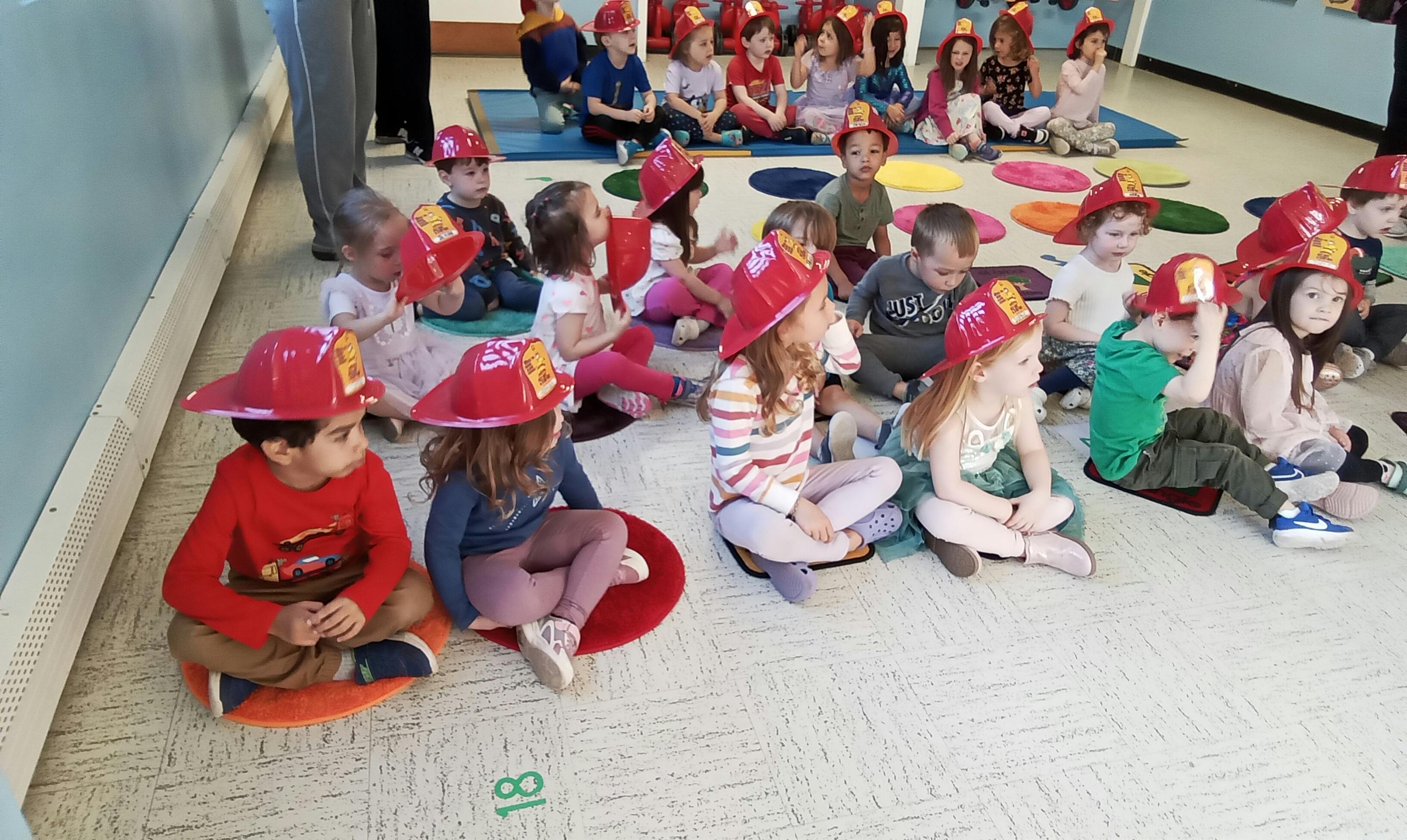 Children wearing red firefighter hats sitting on the floor