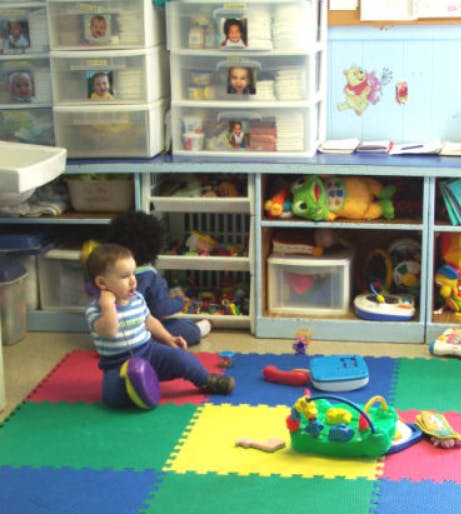 Child sitting on a colorful mat in a room with shelves of toys