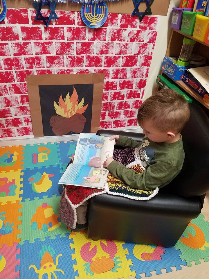 Child sitting in a chair reading a book in a classroom