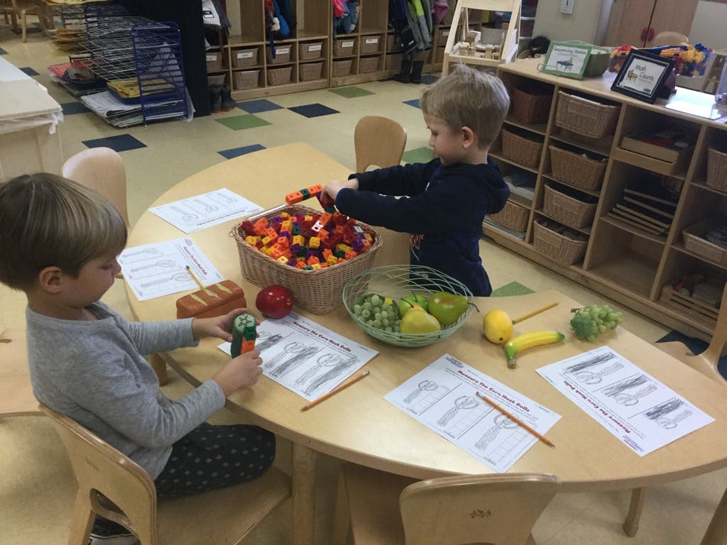 Two children at a table with toys and papers in a classroom