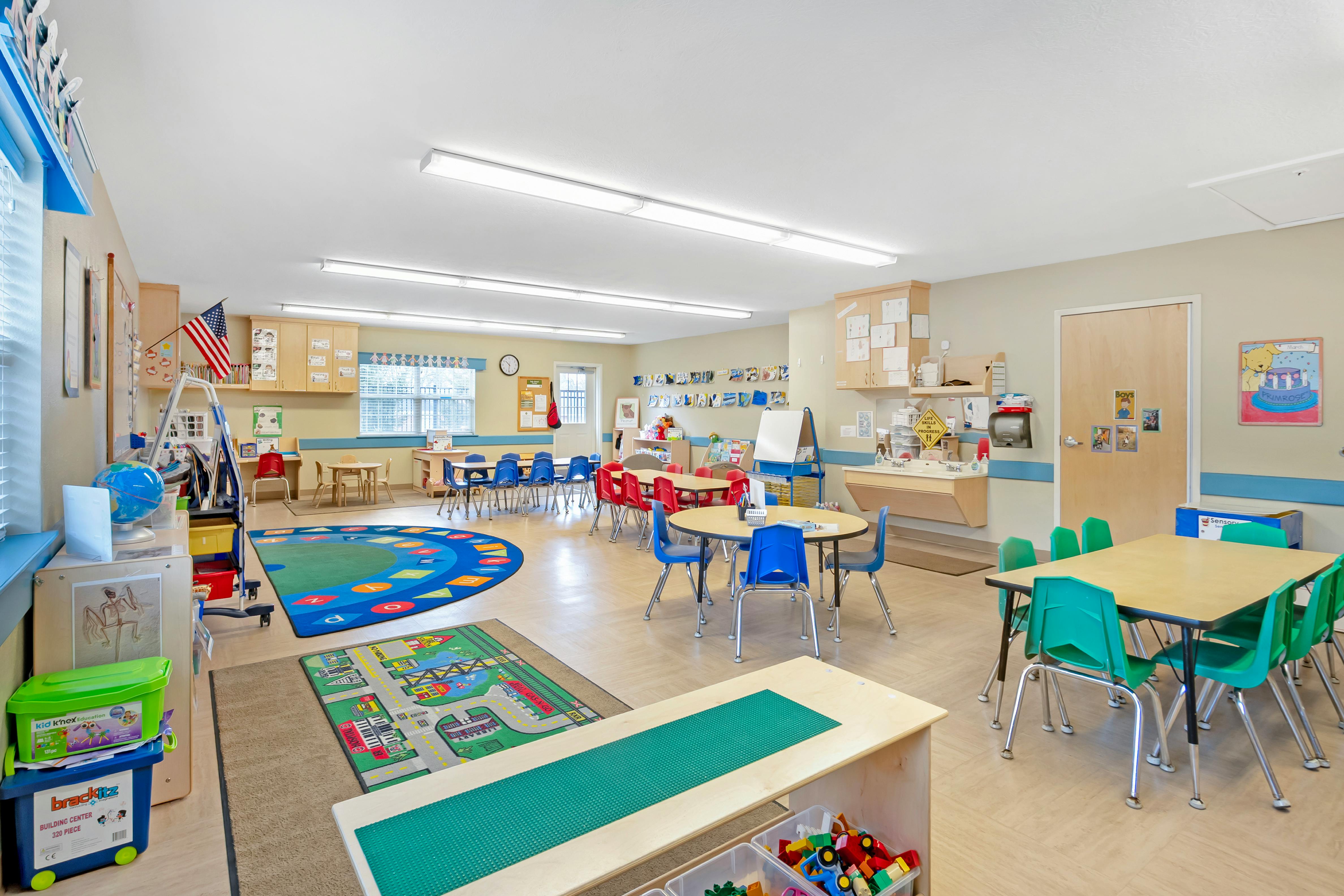Classroom with small tables and chairs, a circular rug with letters, and toys