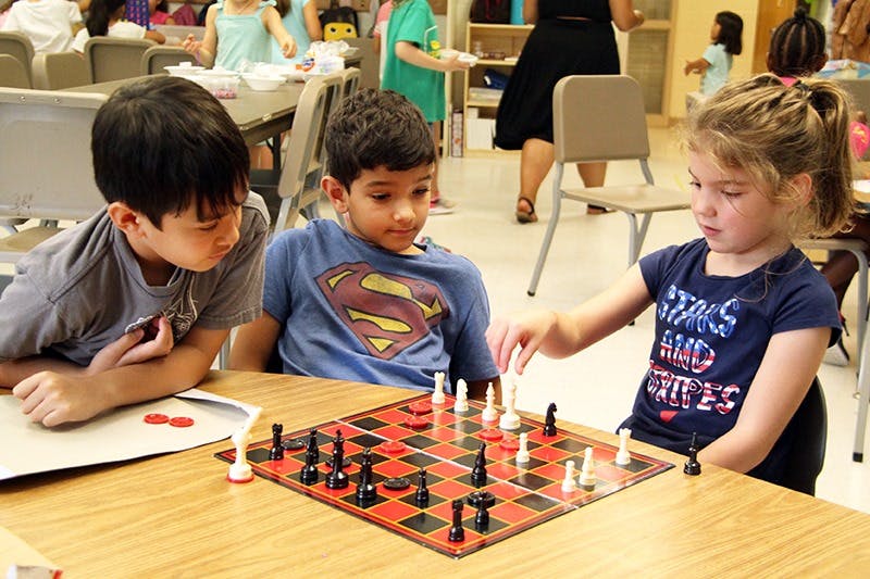 Three children playing chess at a table